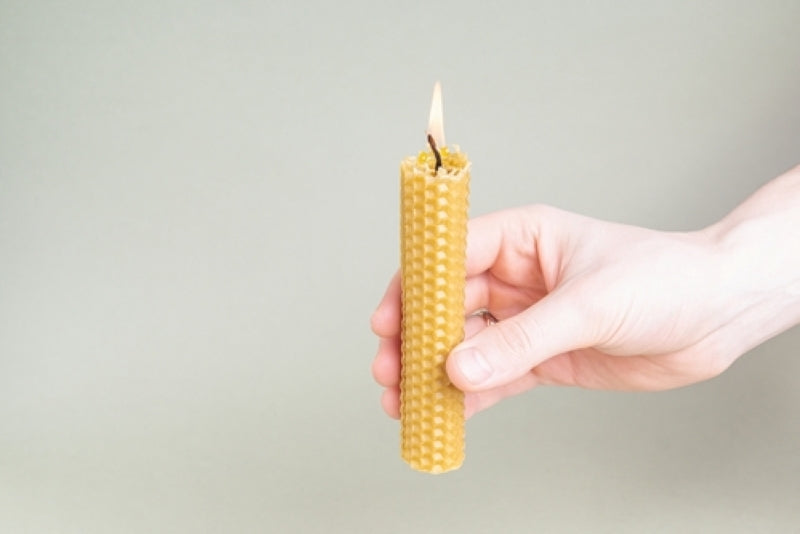 Lit rolled beeswax candle example of one you can make during the beeswax candle making workshop front view